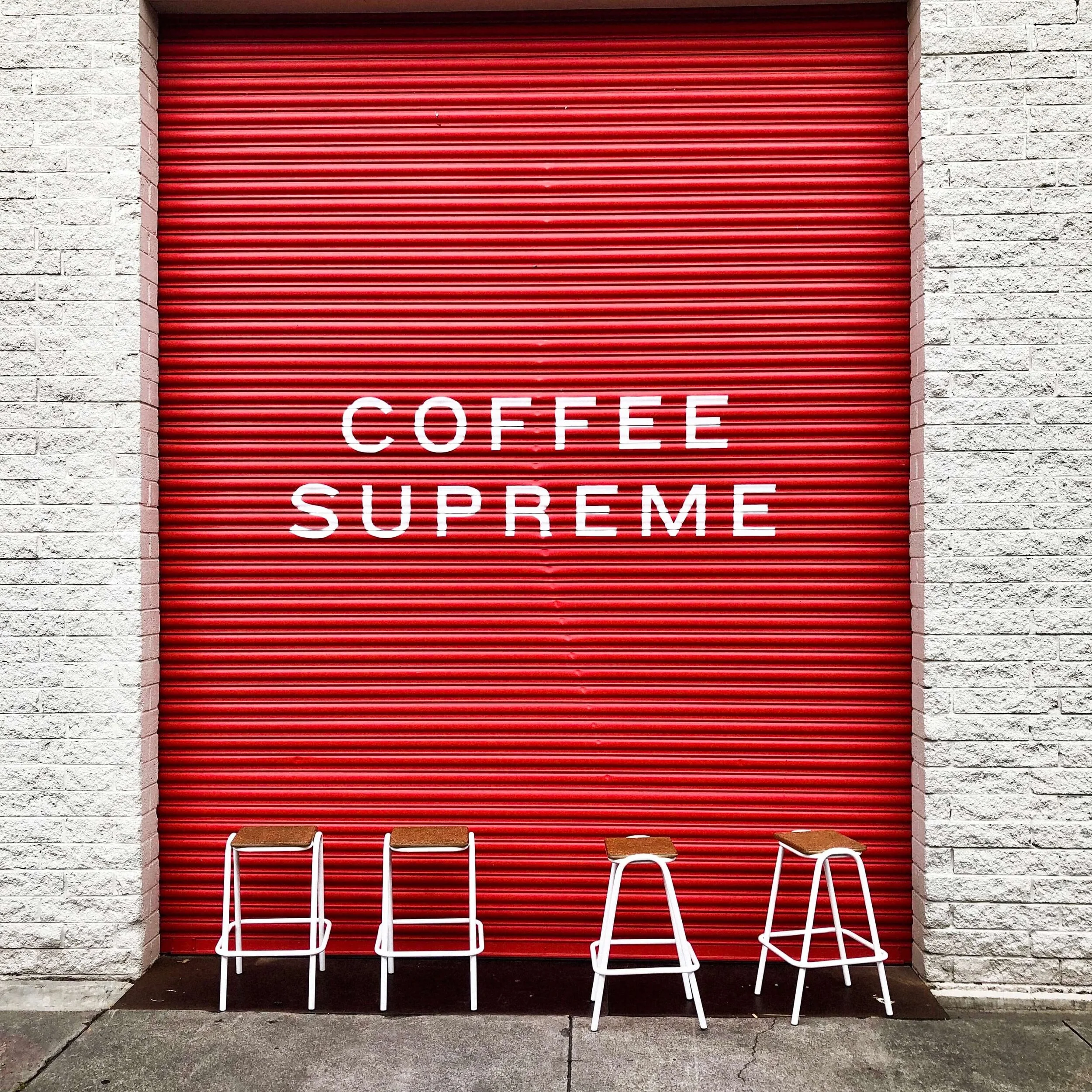 Coffee Supreme sign on a red roller door, with stools lined up in front