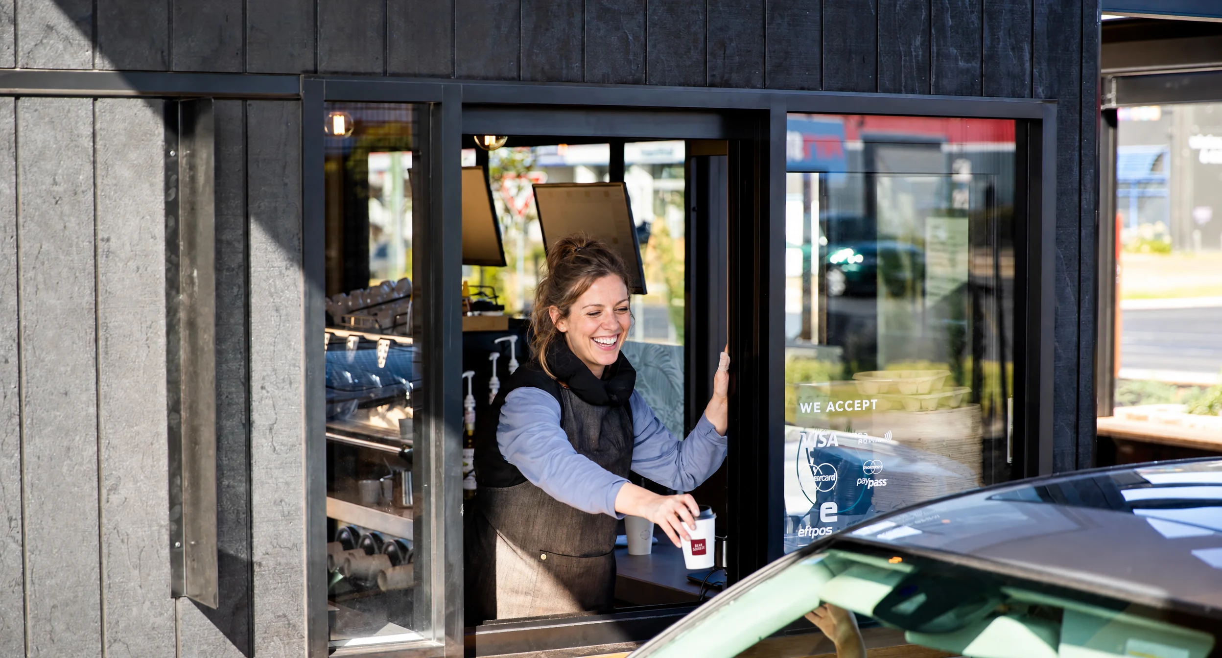 A smiling person handing a Bean Squeeze coffee through the drive-thru window