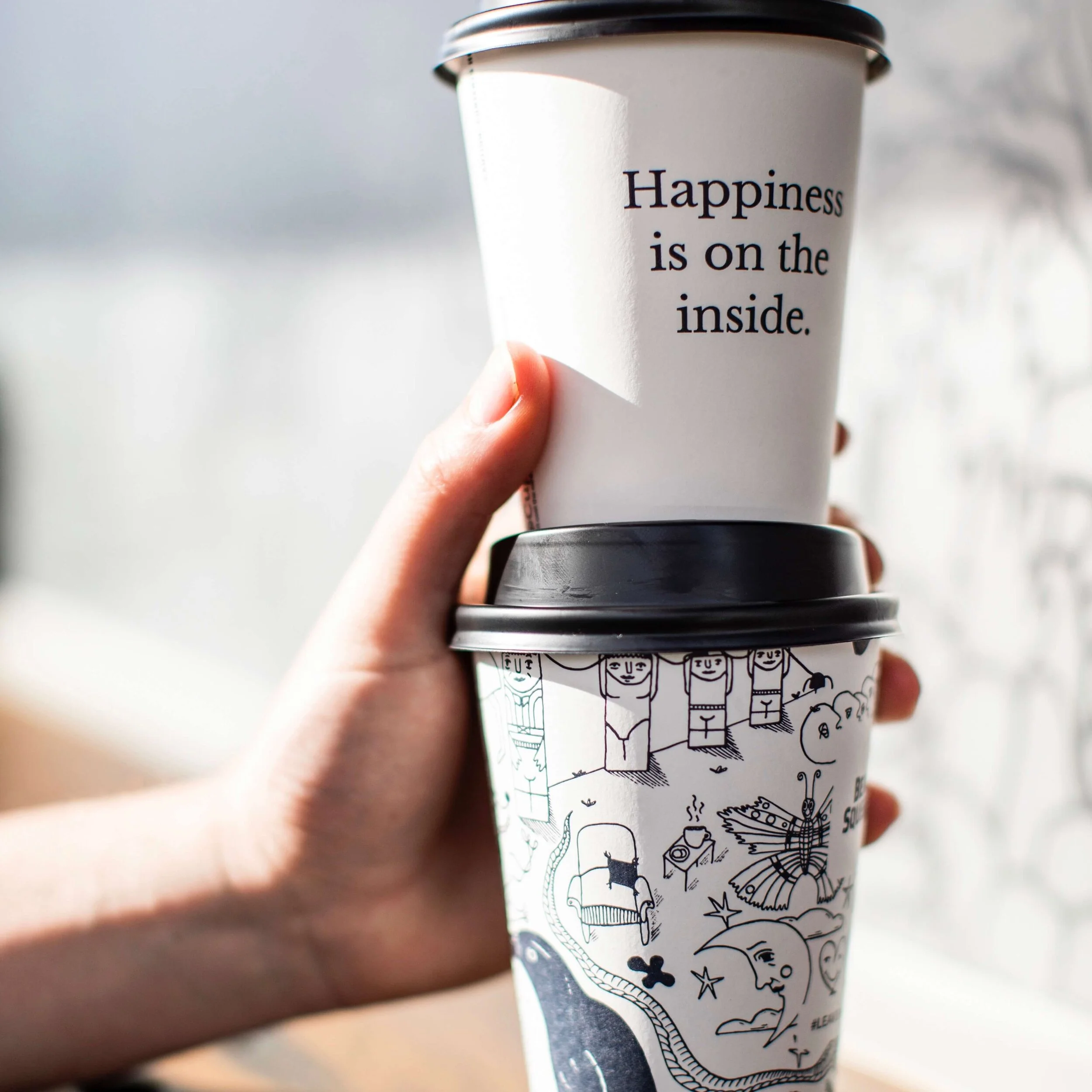 A takeaway cup printed with "Happiness is on the inside" held above another cup