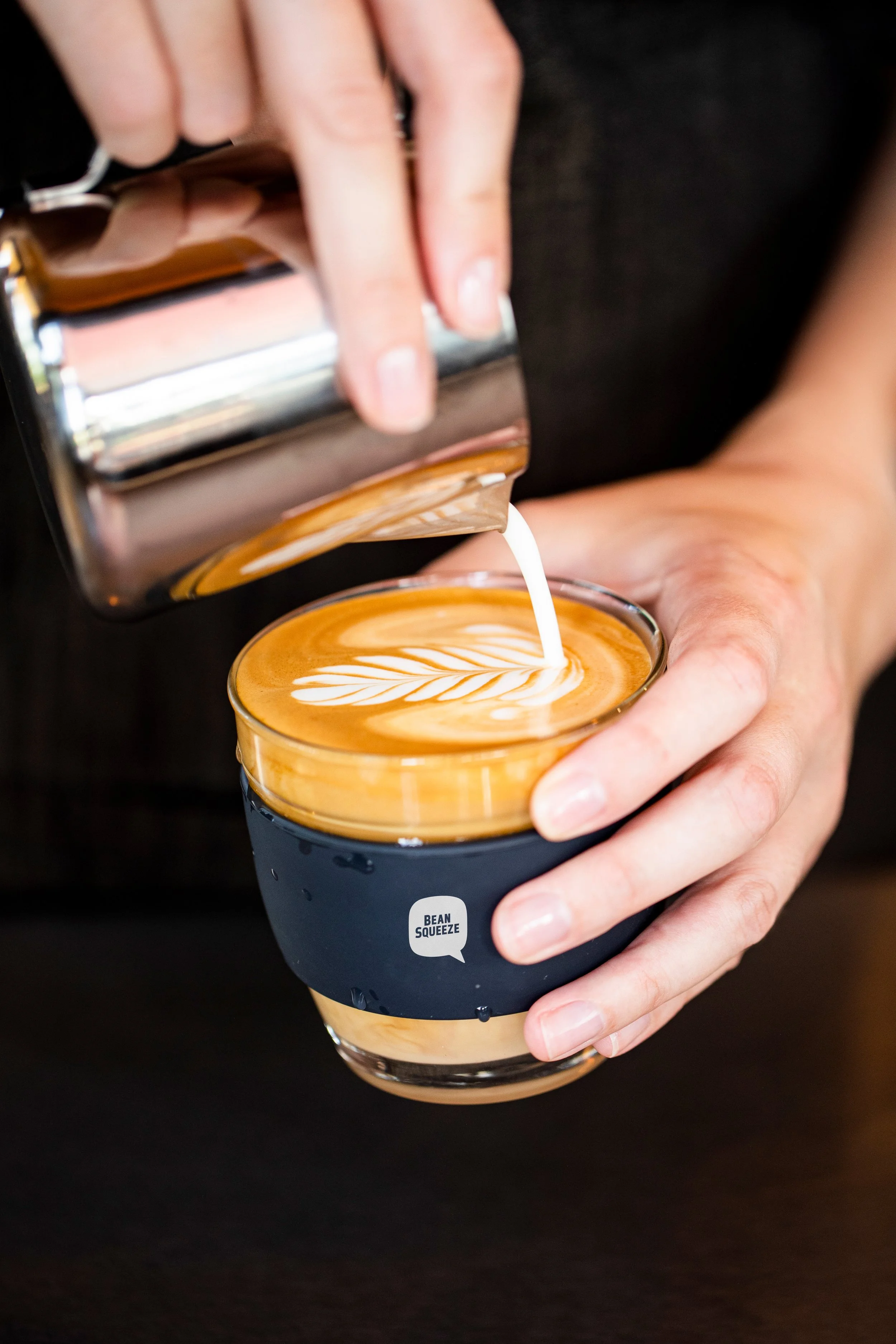 Milk being poured from a jug into a glass cup, forming latte art
